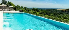 Swimming pool overlooking the green Italian countryside, next to white umbrellas and loungers