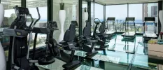 Modern gym with wraparound windows and black treadmills, bikes and cycling machines, plus a glossy floor
