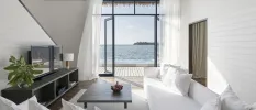 Villa living area with white sofas and walls, a dark-wood coffee table and TV unit and a view of the ocean through open doors