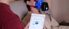 Woman sits in a strapped face mask while a therapist reads a tablet with analysis next to her 