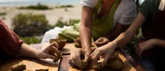 Group of three in aprons making animal figures out of clay with the beach in the background