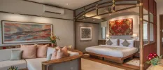 Sleek hotel room with wooden bed and frame, white bedding, wall art with earthy tones, and a neutral cushioned sofa area