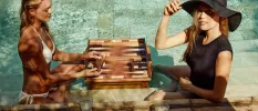 Two woman playing a board game in the swimming pool, one in a white bikini, the other in a black t shirt and floppy hat