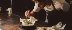 Chef in a dark apron leans over bowls of vegetables