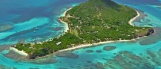 Aerial view of a tropical island cloaked in greenery, circled by white sand and surrounded by turquoise ocean waters
