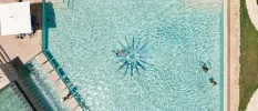 Aerial view of turquoise swimming pool with a star design at its centre, concrete walkway and swimmers enjoying the water in the sunshine