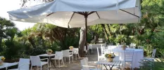 Terrace surrounded by gardens, with white tables and chairs and large parasols