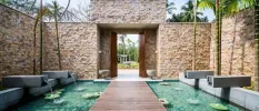 Courtyard with stone walls and a wooden jetty suspended over a pool, with lily pads floating in it
