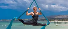 Muscular woman hanging in rope ties in the splits, with the ocean behind her