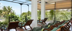 Relaxation area with rows of wooden loungers and wraparound windows overlooking tropical gardens and the Indian Ocean