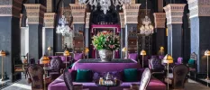 Purple cushioned seating area with other surrounding chairs in a room with a grand chandelier and patterned pillars