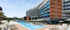Multi-storey glass fronted hotel with an outdoor pool surrounded by white parasols and loungers