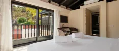 Hotel room with white bedding and cream walls, dark-wood ceiling and doors and a balcony