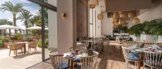 Airy restaurant with indoor and outdoor sections, rattan lantern lighting, blue cushioned chairs and glossy palm trees