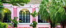 Pink building with large black windows surrounded by tropical greenery and pink flowers