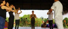 Group in active wear in an open-sided pavilion, with their eyes closed and hands clasped in prayer as an instructor stands at the head of the group