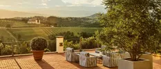 Outdoor terrace with striped armchair-style seating, terracotta-potted plants, and a view of the Tuscan countryside