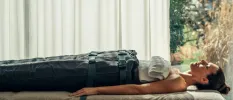 Female lies with her eyes closed on a massage bed in a sleeping bag-style cover