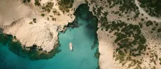 Aerial view of a turquoise cove with a boat, surrounded by cliffs dotted with trees