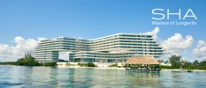 High-rise, multi-storey white resort on a white-sand beach overlooking the sea, under a blue sky with white clouds