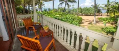 Balcony with wooden chairs and a small table with a fruit basket, with white balustrade overlooking tropical gardens