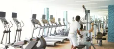 Staff member supports a guest lifting weights in a gym filled with treadmills and step machines