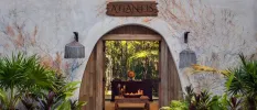 Stone-walled entrance to the Atlantis Spa, with an arched entrance fringed by greenery peering through to a wooden table covered in candles