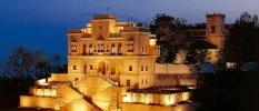 A colonial Indian palace lit up after dark, surrounded by greenery