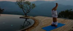 Man in a headstand yoga pose on a blue mat next to an infinity pool with a view of misty hills