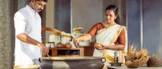 Two staff members in traditional Indian dress work over a large pot surrounded by pots of herbs