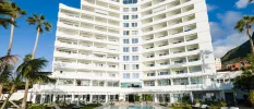 High-rise white hotel, swimming pool and palm trees under a blue sky