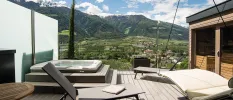 Wooden terrace with a hanging bed, loungers, hot tub and a sauna overlooking the mountains and valley below