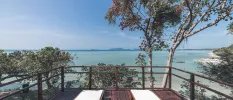 Wood-decked balcony with two white loungers overlooking the sea and surrounding greenery