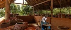 Open-air thatched pavilion filled with terracotta pottery, and a Sri Lankan man shaping a pot on a wooden table in the centre