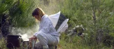 Woman in white bent over a steaming pot among lush countryside