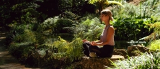 Woman in black leggings and white top sitting on a rock meditating 