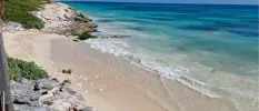 White sandy beach with turquoise shallows backed by rocks and greenery under a blue sky