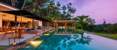Infinity pool lined with lit lanterns and surrounded by blue cushioned loungers and jungle greenery