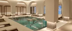 Square indoor pool with central fountains, a softly lit terrace with wooden daybeds and loungers with white cushions