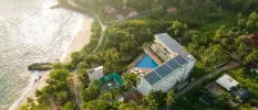 Resort topped with solar panels and surrounded by tropical greenery, with a triangle shaped pool and a beachfront location