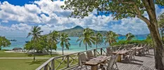 Outdoor restaurant terrace with wooden flooring, trees and a view of a lawn and ocean with mountains in the distance