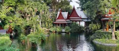 Temple-like buildings look over a lake with a wooden bridge and open-air pavilion either side