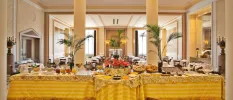 Airy restaurant with tall pillars and a long table with a gold tablecloth, laid up with breakfast options including jars of juices, bowls of cereal and baskets of pastries