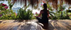 Woman in black active wear meditates among tropical gardens overlooking the sea and mountains