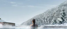 Woman at the edge of a heated pool, overlooking a snowy forested mountain