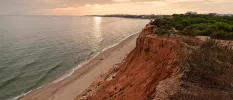Golden sandy beach backed by red cliffs topped with greenery
