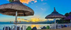 Beachfront bar on the sands, with thatched umbrellas, white wooden chairs and blue and green bean bags at sunset