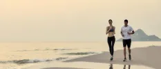 Man and woman in active wear jog across the sand as the sun comes up, with a mountain in the background