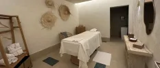 Treatment room with white walls adorned with straw hats, a massage bed covered in white cloth 