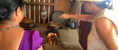 Two women standing over traditional pots on a fire, stirring some food